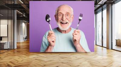 Photo of positive smiling grandfather hold cutlery wear light blue t-shirt isolated over violet color background Wall mural