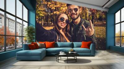 Photo of positive swag two people students couple make selfie show horned symbol in autumn city urban park wear jacket sunglass Wall mural