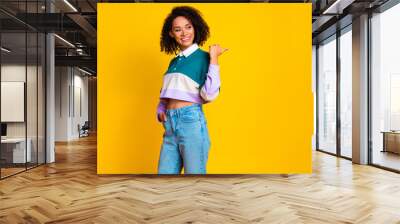 Photo of positive woman with curly hair dressed striped top look directing at proposition empty space isolated on yellow color background Wall mural