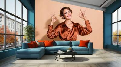 Photo of pretty adorable woman wear silky blouse showing two okey signs smiling isolated beige color background Wall mural