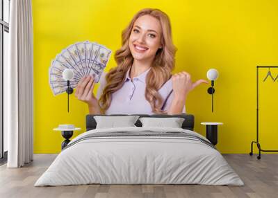 Photo of pretty cute woman dressed violet t-shirt rising cash fan thumb empty space isolated yellow color background Wall mural