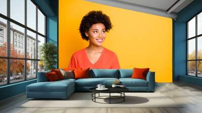 Photo of pretty dark skin lady looking empty space with interest wear orange v neck t-shirt isolated yellow color background Wall mural