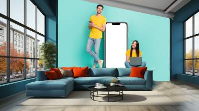 Photo of pretty dreamy married couple wear yellow t-shirts texting looking modern gadget empty space isolated teal color background Wall mural