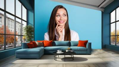 Photo of pretty lady good mood finger on cheek look up empty space think wear white shirt isolated blue color background Wall mural