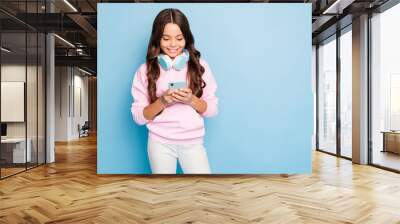 Photo of pretty little lady holding telephone hands turning on new popular youth song in wireless earflaps wear casual hoodie pink pullover isolated blue color background Wall mural