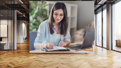 Photo of pretty young girl sit desktop pc hold pen write notepad wear glasses shirt in home office indoors Wall mural