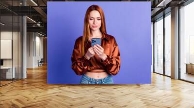 Photo of pretty young woman use smart phone empty space wear brown shirt isolated on violet color background Wall mural