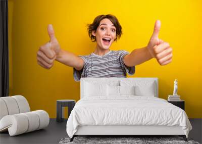 Photo of satisfied good mood funny woman dressed striped t-shirt two hands showing thumbs up to you isolated on yellow color background Wall mural