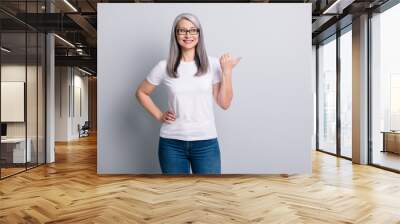 Photo of senior lady direct thumb look empty space wear glasses jeans white t-shirt isolated grey color background Wall mural