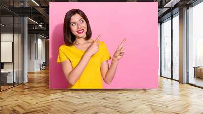 Photo of shiny charming young lady dressed yellow clothes smiling pointing two fingers empty space isolated pink color background Wall mural