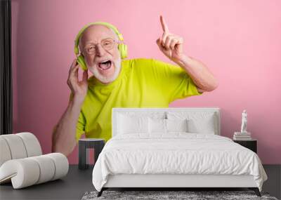 Photo of singing optimistic old man listen music dance wear headphones spectacles lime color clothes isolated on pink background Wall mural