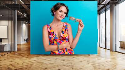 Photo of smart intelligent woman with short hairstyle dressed colorful clothes arm holding glasses isolated on blue color background Wall mural