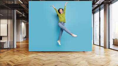 Photo of surprised crazy funky lady jump raise hands wear green shirt jeans sneakers isolated blue color background Wall mural