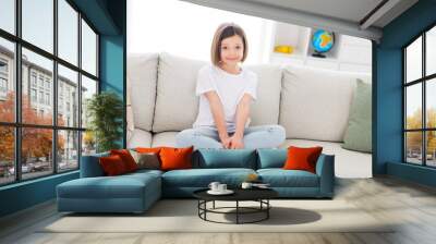 Photo of sweet adorable small schoolgirl dressed white t-shirt sitting coach legs crossed indoors room home house Wall mural