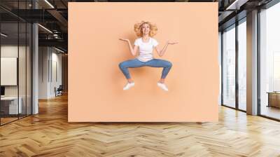 Photo of sweet adorable young lady wear white t-shirt smiling jumping high compare arms empty space isolated beige color background Wall mural