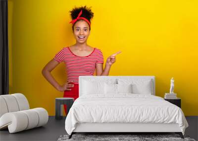 Photo of sweet excited girl dressed red striped t-shirt open mouth pointing finger empty space isolated yellow color background Wall mural