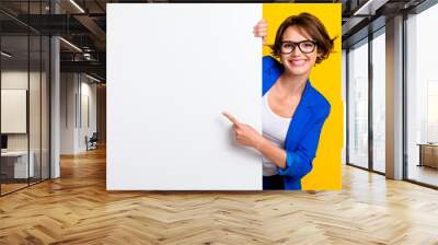 Photo of sweet shiny woman wear blue jacket spectacles pointing white wall poster empty space isolated yellow color background Wall mural