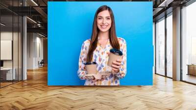 Photo of sweet shiny young lady wear print shirt smiling holding coffee inviting you drinking isolated blue color background Wall mural