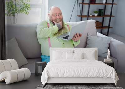 Photo of thoughtful young man sit on couch arm on chin look interested laptop thinking free time indoors Wall mural