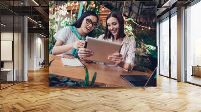 Photo of two attractive cheerful students girls hold tablet chatting working cafe indoors Wall mural