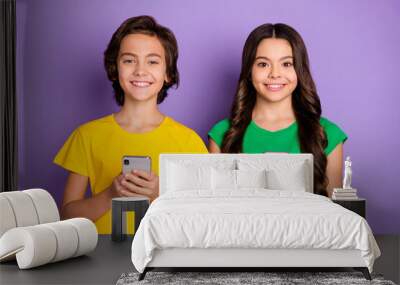 Photo of two happy positive little children hold phone comment post smile isolated on violet color background Wall mural