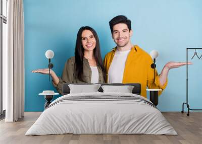 Photo of two nice young partners hold empty space vs wear shirt isolated on blue color background Wall mural