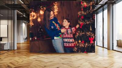 Photo of two peaceful people mother daughter hang toys tree hug new year xmas garland lights apartment indoors Wall mural