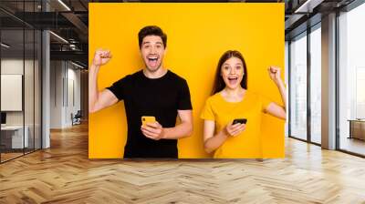 Photo of two students guy lady holding telephones reading good news celebrating online network money income wear casual black t-shirts isolated yellow color background Wall mural