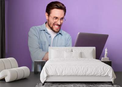 Photo of unhappy angry young man look hold laptop write letter work isolated on purple color background Wall mural