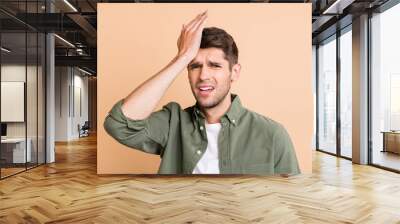 Photo of unhappy upset young man hold hand head ache pain suffer isolated on pastel beige color background Wall mural