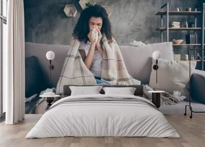 Photo of unhealthy dark skin wavy lady suffering flu caught cold sneezing paper napkins everywhere sitting couch covered plaid blanket living room indoors Wall mural