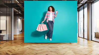 Photo of wavy hair young woman in stylish casual clothing holding shopping bags with favorite coffee isolated on aquamarine color background Wall mural