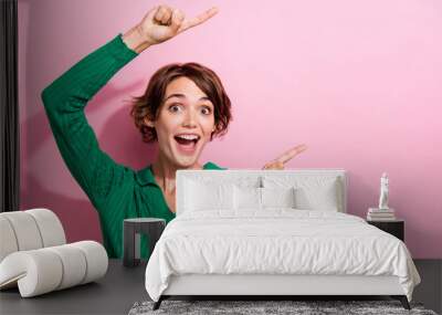 Photo of young astonished woman wear stylish shirt directing finger empty space unexpected information isolated on pink color background Wall mural