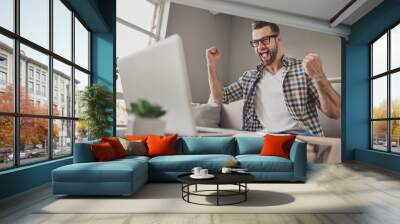 Photo of young excited man happy positive smile celebrate win victory success fists hands sit sofa home remote work Wall mural