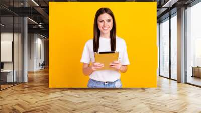 Photo of young girl happy positive smile hold tablet gadget virtual isolated over yellow color background Wall mural