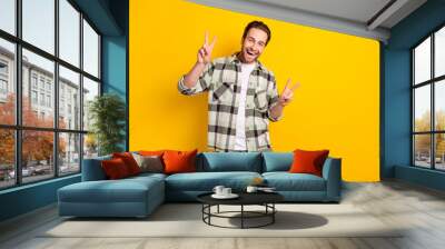 Photo of young handsome man happy positive smile show hello peace cool v-sign isolated over yellow color background Wall mural