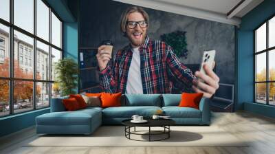 Photo of young successful businessman wearing checkered shirt holding coffee to go photographing his day at office indoors Wall mural