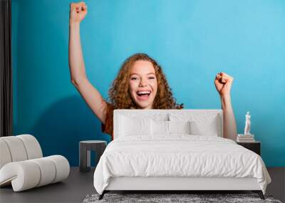 Photo of young successful red haired girl in orange t shirt raised fists up celebrating boyfriend winning isolated on blue color background Wall mural