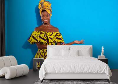 Photo of young sweet smiling african woman advertising product showing options isolated on blue color background Wall mural