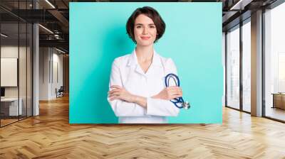 Photo of young woman happy positive smile crossed hands hold stethoscope doctor isolated over teal color background Wall mural