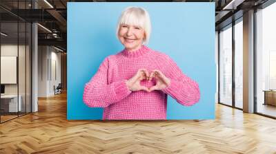 Photo portrait of cheerful elderly woman showing heart with fingers on chest isolated on pastel blue colored background Wall mural