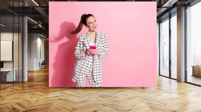 Photo portrait of funky girl looking at blank space holding phone in two hands isolated on pastel pink colored background Wall mural