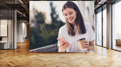 Photo portrait of girl holding phone paper cup smiling outdoors Wall mural