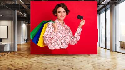 Photo portrait of girl with shopping bags holding credit card isolated on bright red colored background Wall mural