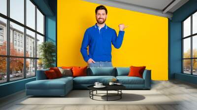 Photo portrait of handsome young guy point empty space dressed stylish blue garment isolated on yellow color background Wall mural