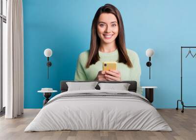 Photo portrait of happy woman holding phone in two hands isolated on pastel blue colored background Wall mural