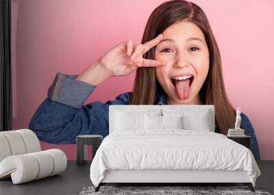 Photo portrait of little girl showing v-sign gesture smiling showing tongue isolated on pastel pink color background Wall mural