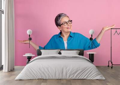 Photo portrait of lovely pensioner lady compare look hold empty space dressed stylish blue garment isolated on pink color background Wall mural