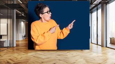 Photo portrait of lovely pensioner lady look point amazed empty space dressed stylish yellow garment isolated on dark blue color background Wall mural