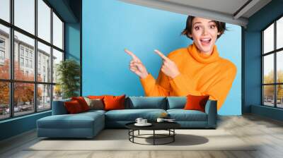 Photo portrait of lovely young lady fingers point empty space excited funky wear trendy orange garment isolated on blue color background Wall mural